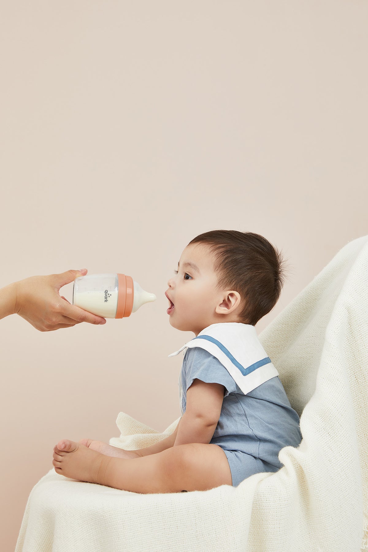 Adult feeding infant BuubiBottle Mini orange hybrid bottle while baby sits on lap