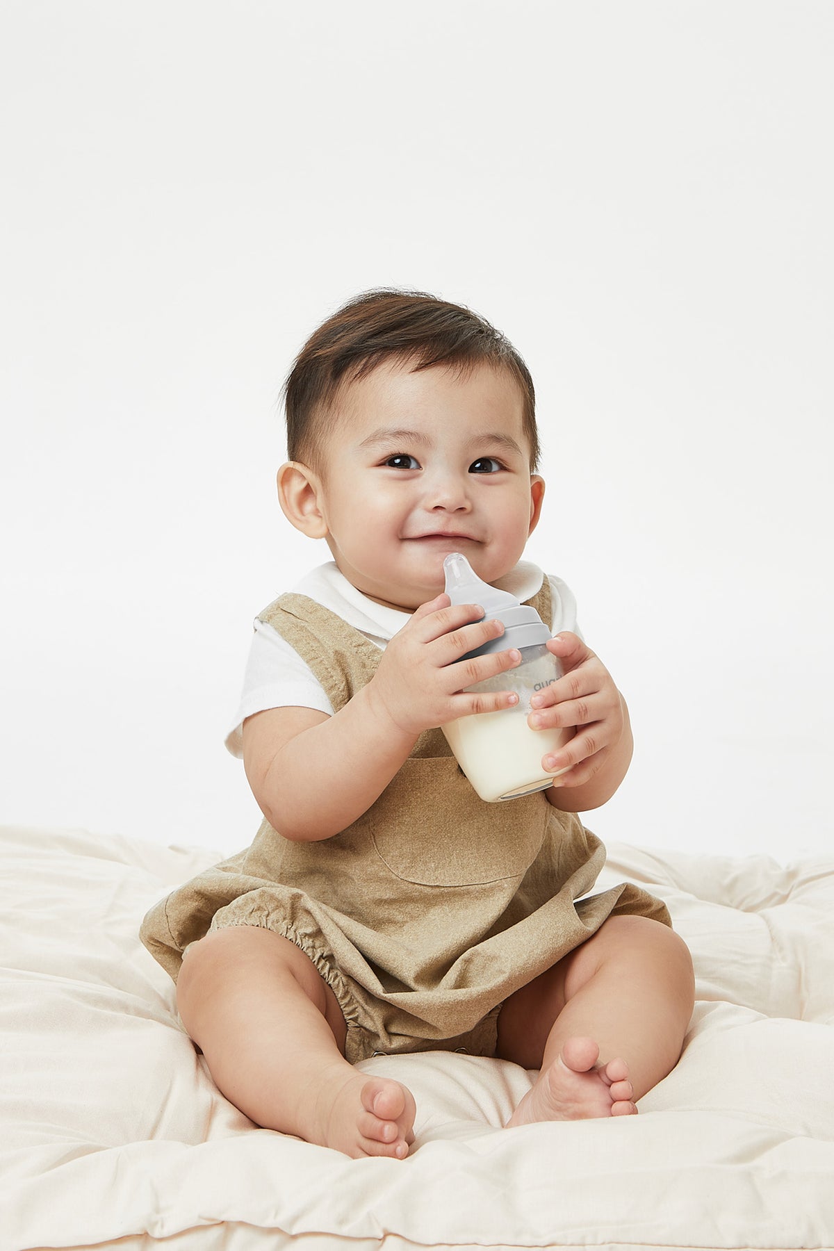Smiling infant holding BuubiBottle Mini grey 5oz feeding bottle — shatterproof baby bottle safe for self-feeding, anti-colic design
