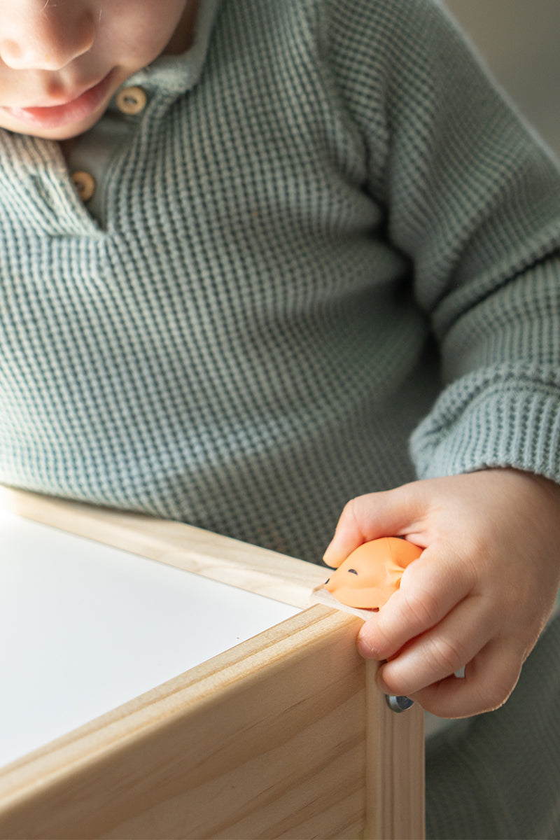 Toddler hand touching Quark Foxii silicone corner protector on wooden furniture edge