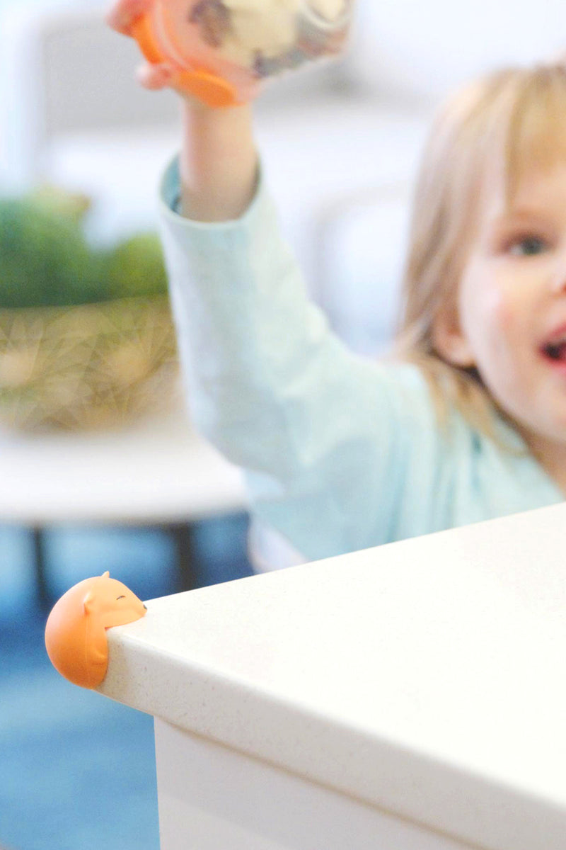 Toddler reaching toward Quark Foxii orange fox-shaped corner protector on table edge