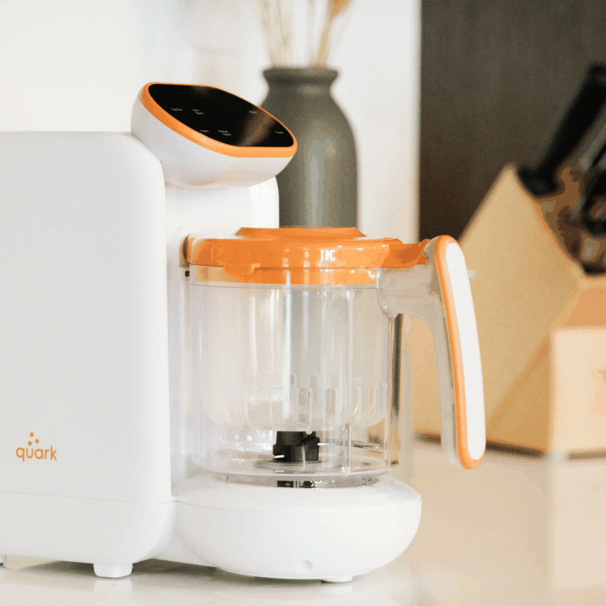 Quook baby food maker with orange accent lid on kitchen counter — compact 5-in-1 steamer blender for homemade baby food and bottle warming