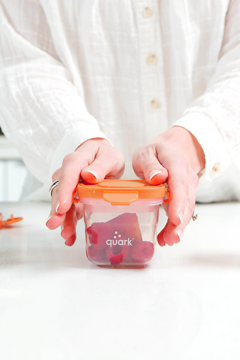 Adult hands holding Quark Storii baby food storage container with clip-in ice pack, lifestyle shot
