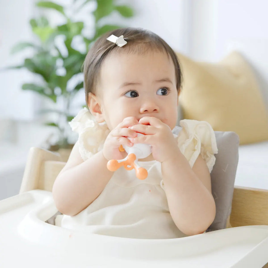 Quark Baby teething toy with orange details, infant holding and chewing during solids introduction stage