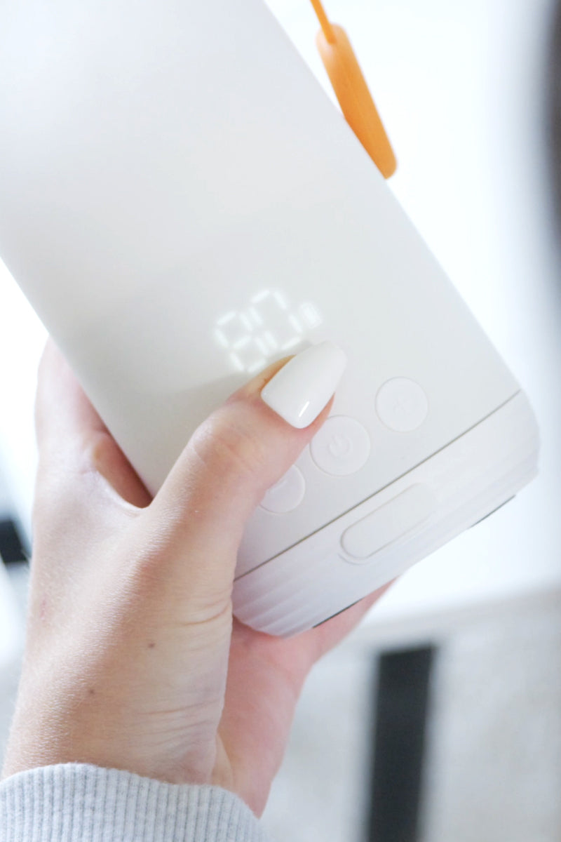 BuubiBottle Portable Milk Warmer PRO held in one hand, display lit