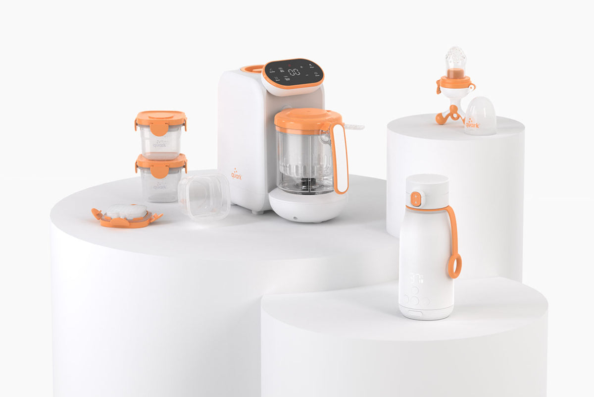 Quark Baby innovative feeding accessories collection with orange accents displayed on white pedestals.