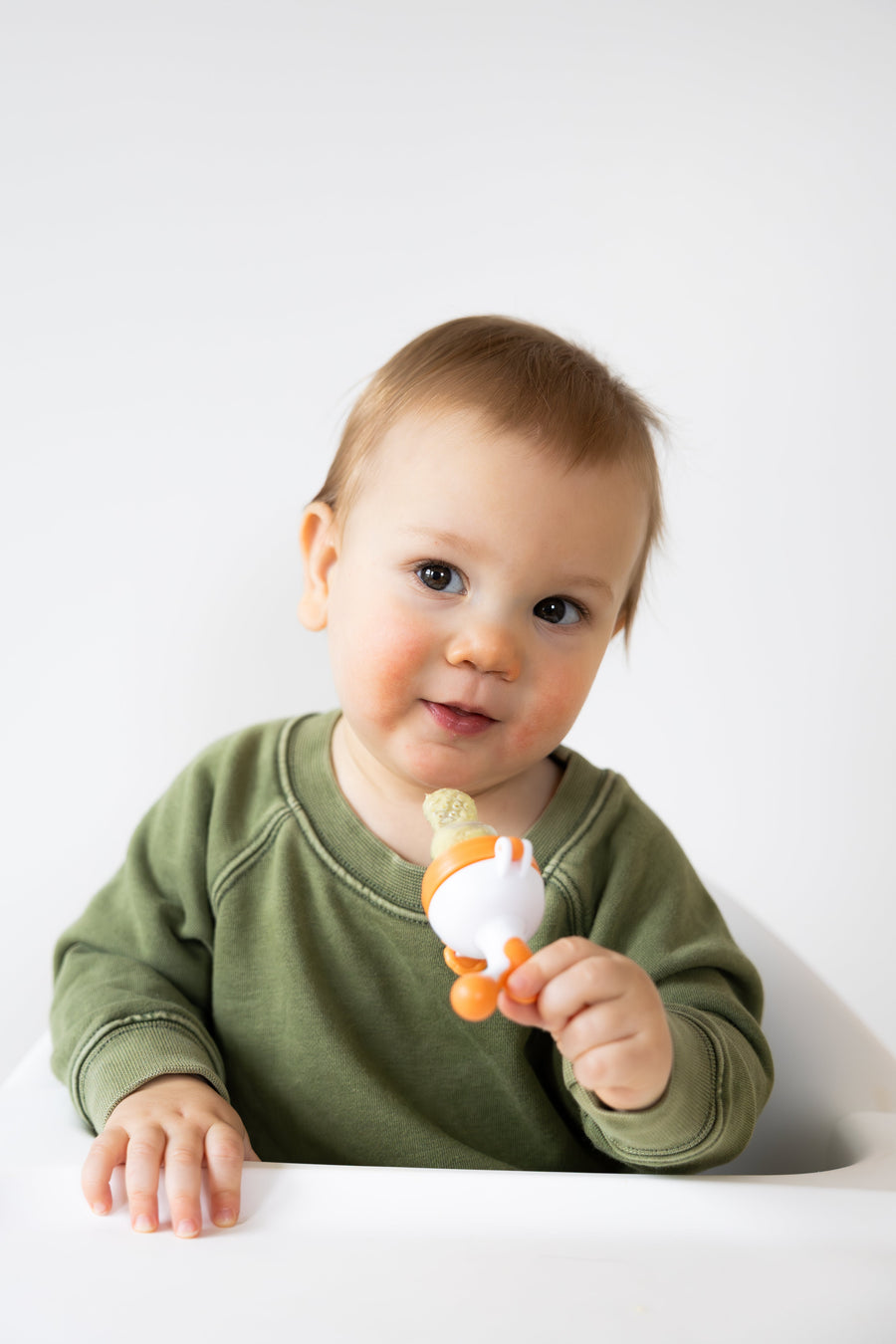 Toddler holding Quark Baby Fruuti fruit feeder during a supervised first-foods routine