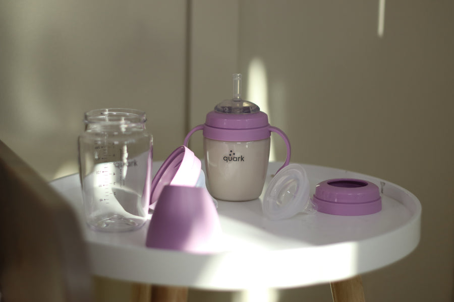 Quark Baby purple sippy cup with handles and accessories on white table.
