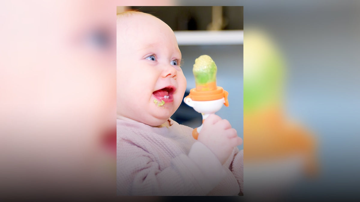Baby seated upright holding a Fruuti silicone fruit feeder