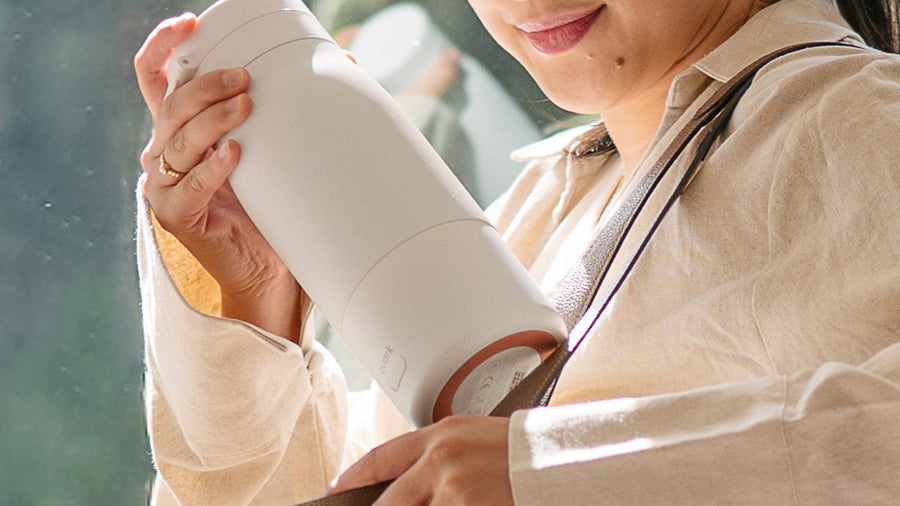 Parent slipping the BuubiBottle PRO portable milk warmer into a tote bag before heading out