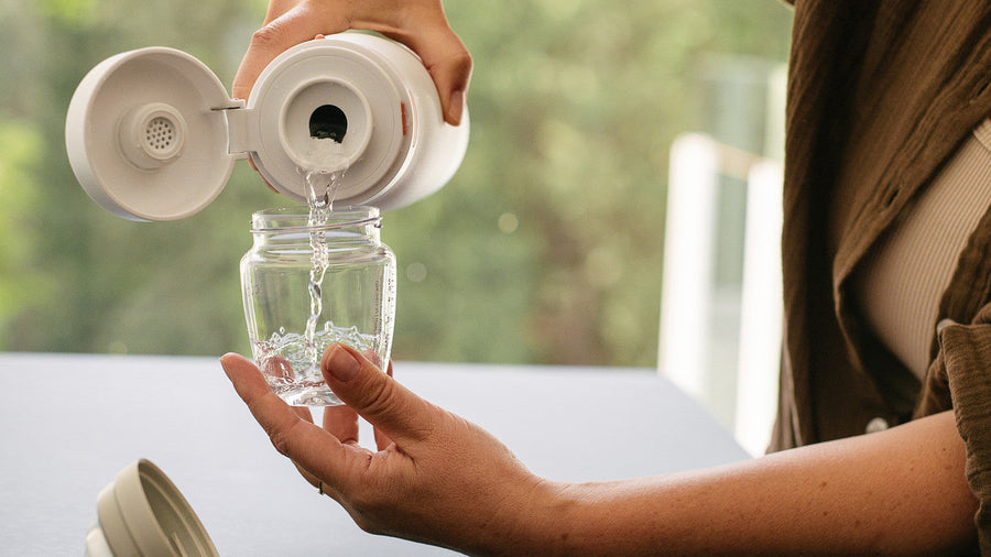 BuubiBottle Portable Milk Warmer PRO with the cap open, rinsing the stainless steel vessel with clean water