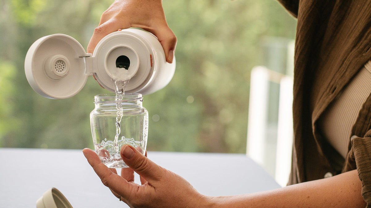 Pouring from the open BuubiBottle Portable Milk Warmer PRO vessel at the kitchen counter