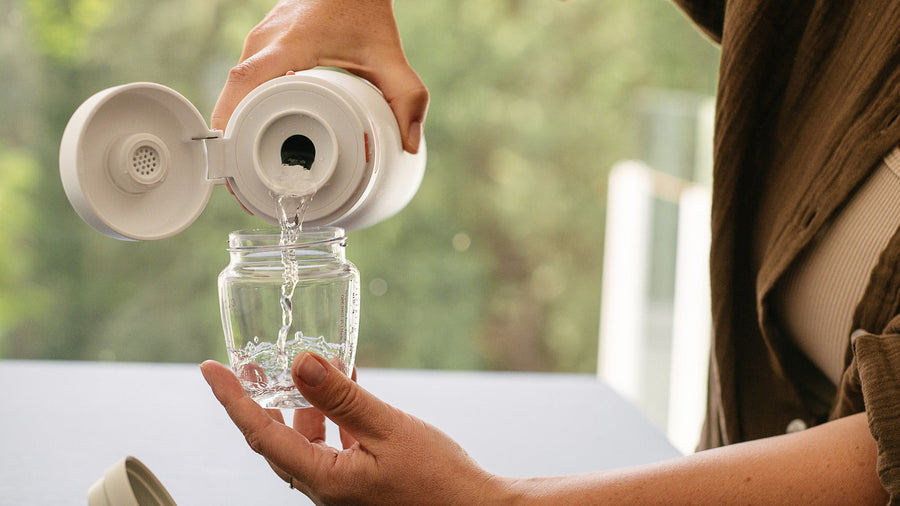 Pouring from the open BuubiBottle Portable Milk Warmer PRO vessel at the kitchen counter