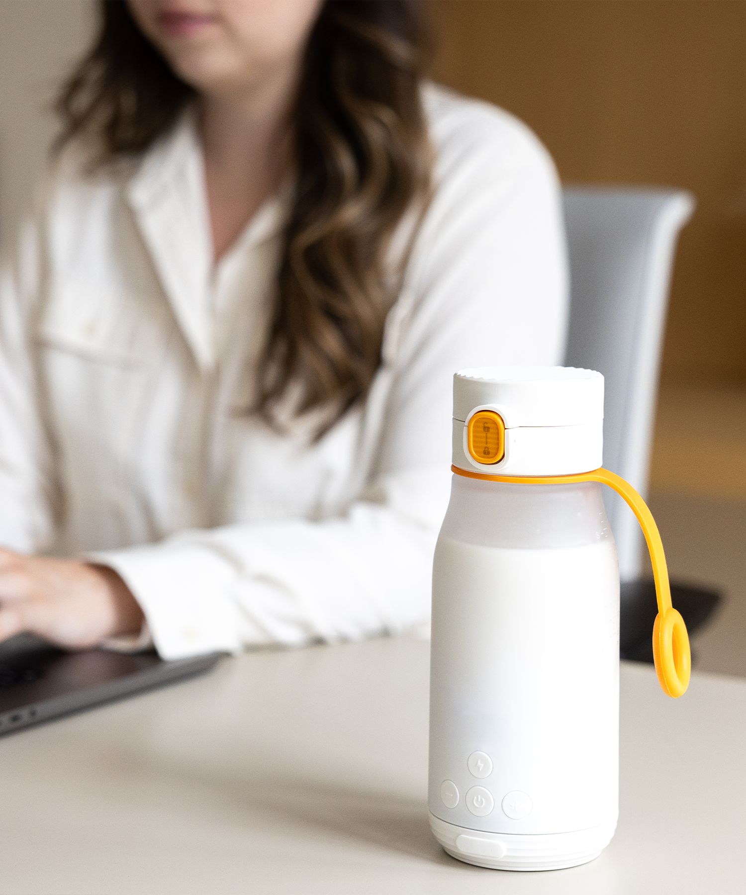 Quark Baby white bottle with yellow handle sitting on desk beside woman in white shirt working