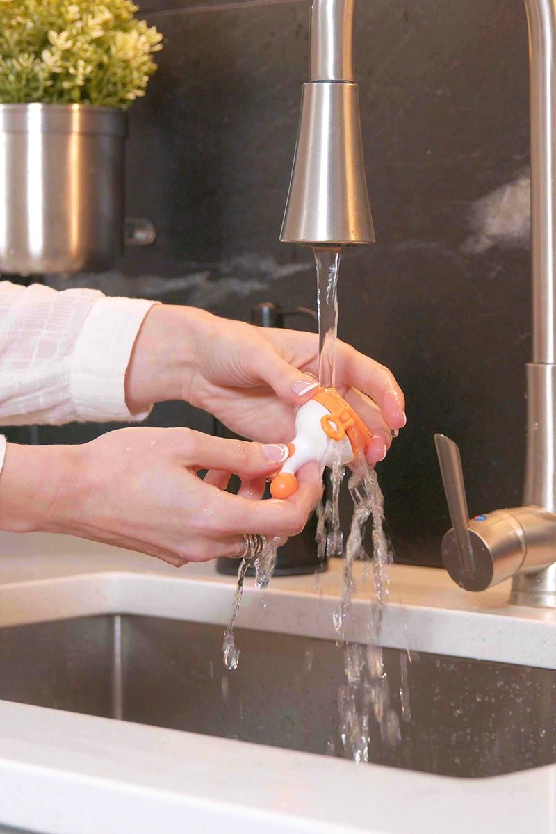 Adult hands rinsing Quark Fruuti baby food feeder under running water at kitchen sink.