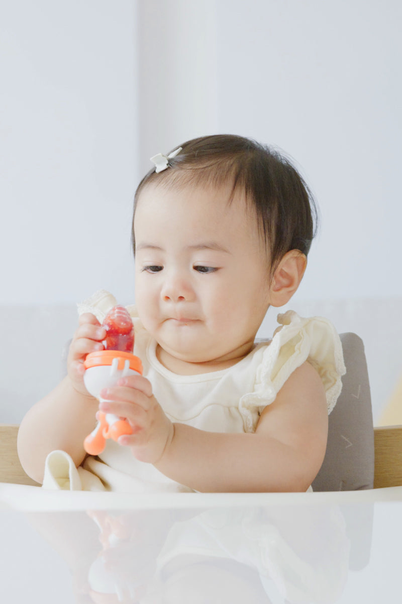 Toddler holding Quark Fruuti baby food feeder with twist-eject silicone tip design