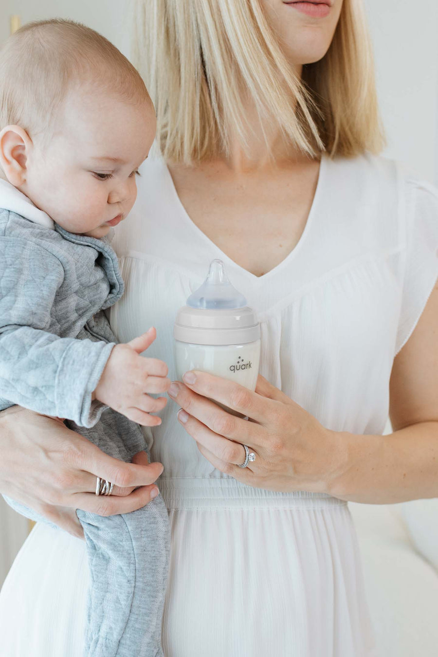 Mother holding newborn while offering BuubiBottle Mini 5oz grey bottle — best baby bottles for breastfed babies starter set