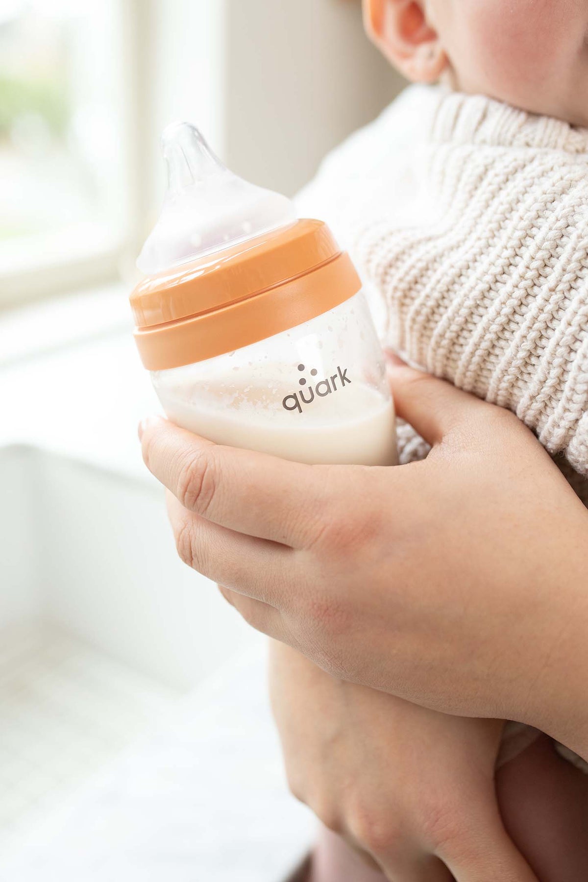 Adult hand holding Quark BuubiBottle with milk and nipple, lifestyle feeding shot