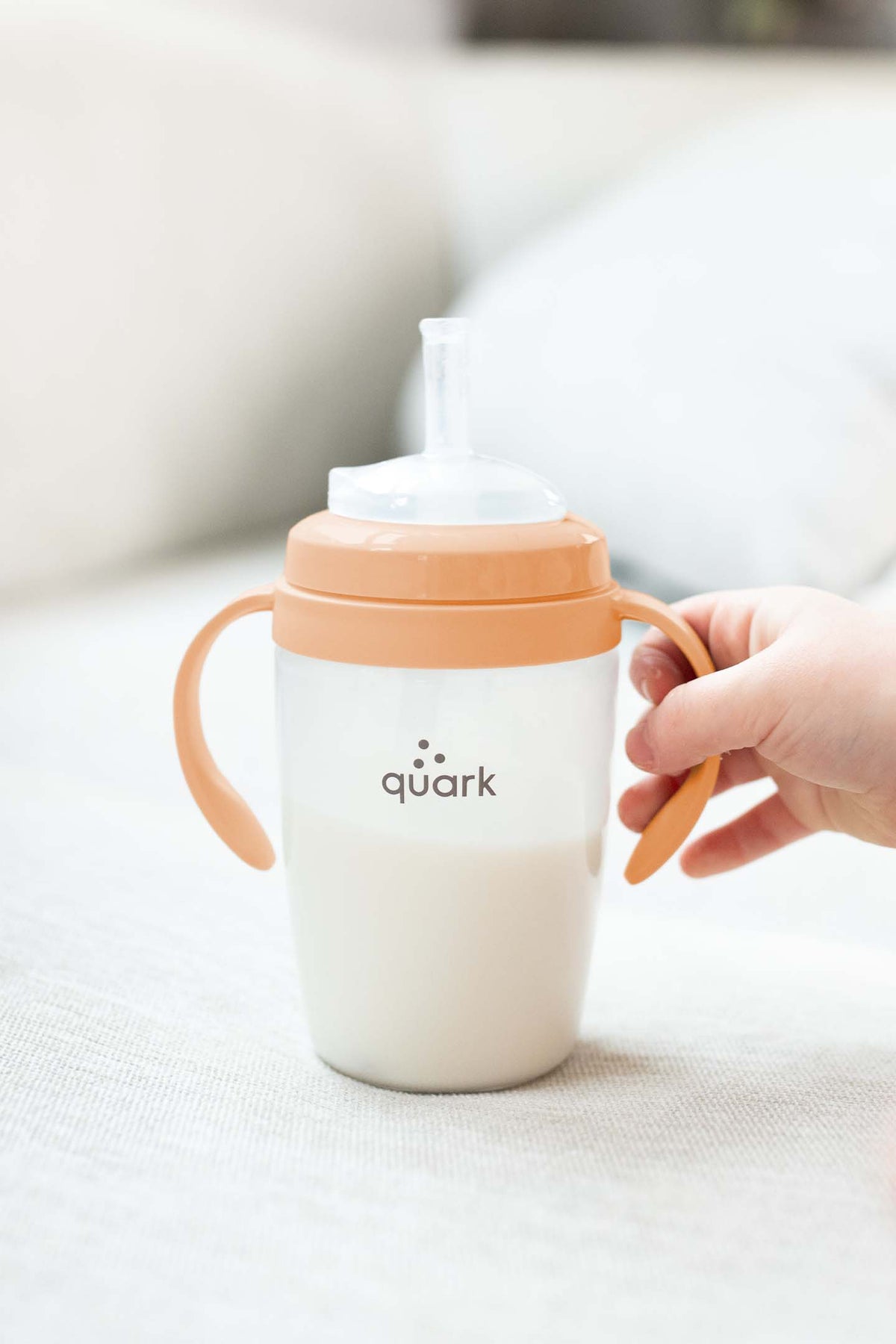 Quark BuubiBottle Sip conversion kit with orange handles and white body, held by child's hand against neutral background