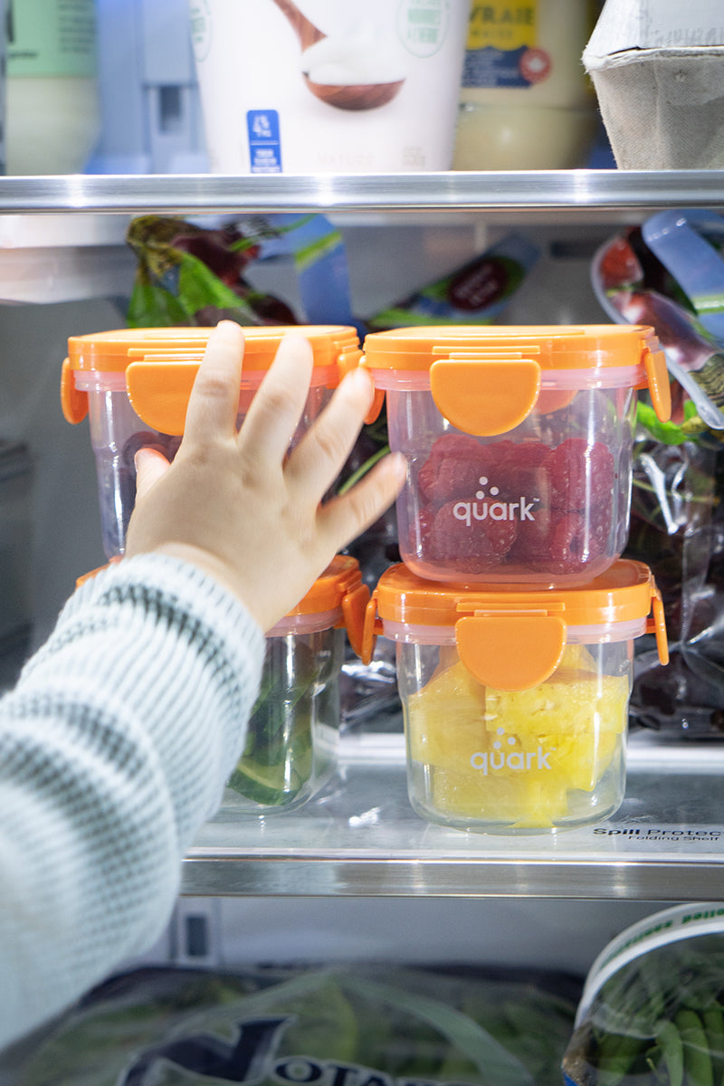 Child's hand reaching for Quark Storii baby food storage containers in refrigerator