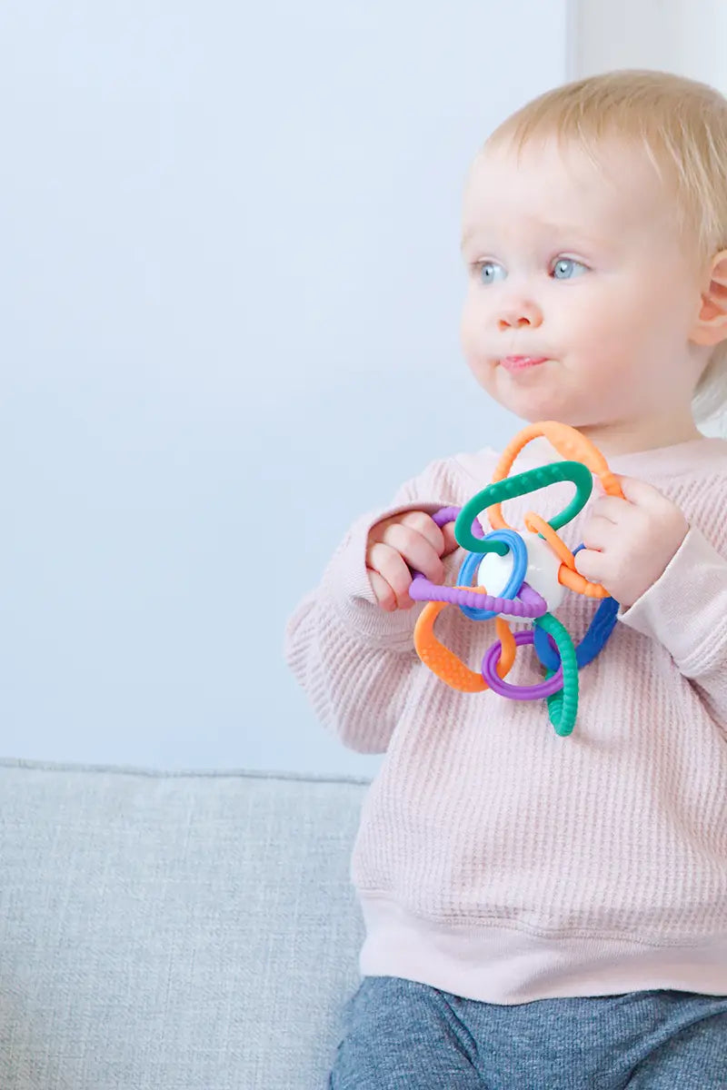 Toddler holding colorful Quark Thiingy sensory teether toy for tactile exploration